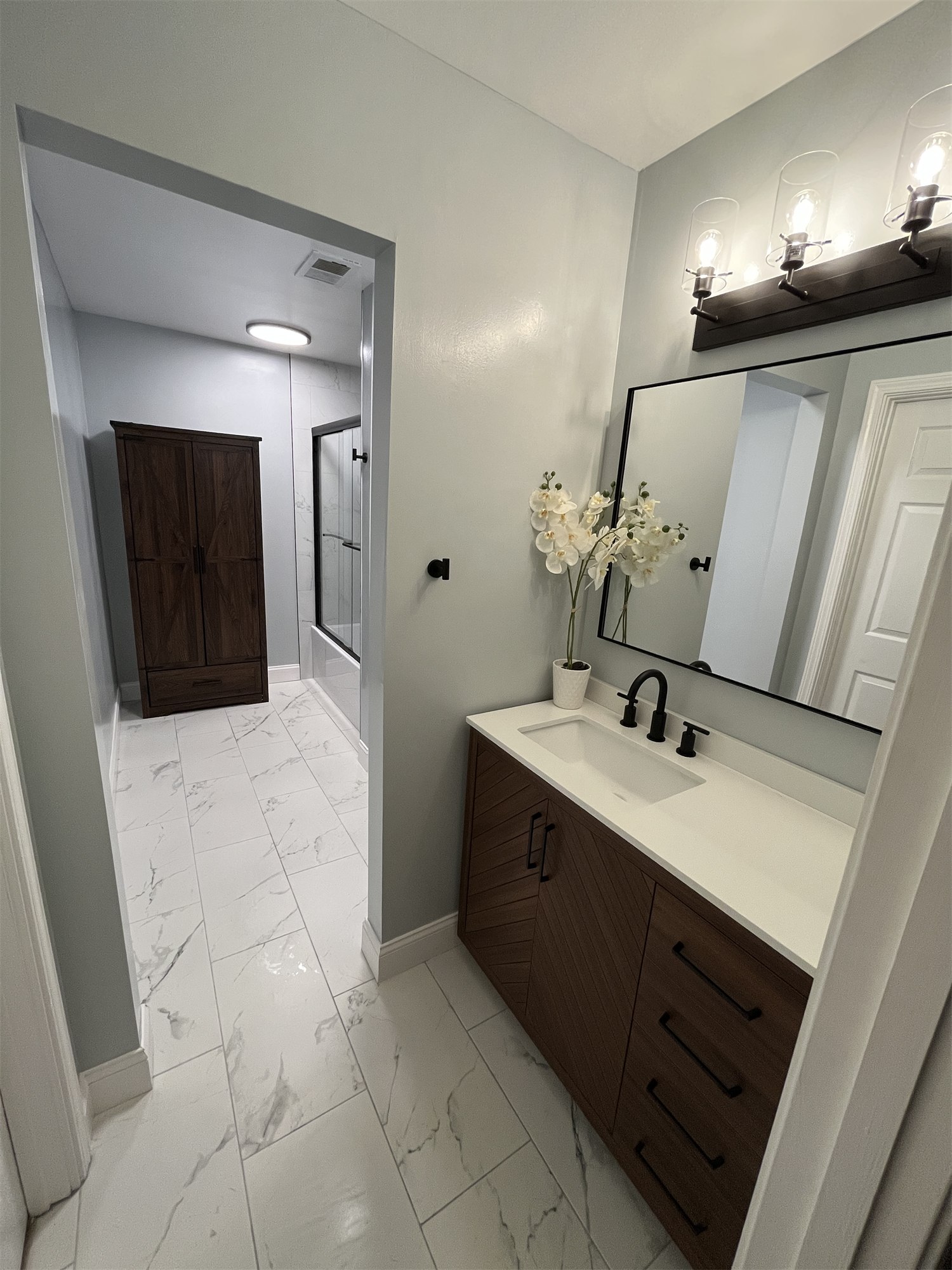 Completed bathroom with white tile, a dark vanity, and a glass shower enclosure